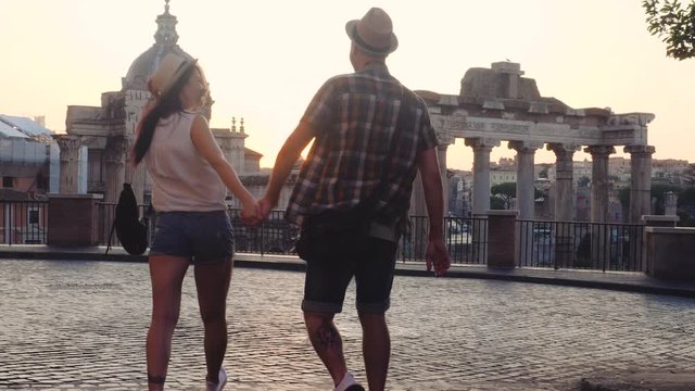 Young couple tourist walking towards Roman Forum at sunrise. Historical imperial Foro Romano in Rome, Italy from panoramic point of view.