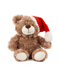little cute brown teddy bear with in a red Christmas hat sits