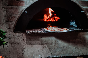 Italian chef is putting prepared margarita pizza to the oven with flame in it.
