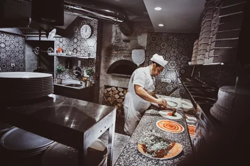Poster Italian chef in uniform is adding tomato sauce for pizza at the kitchen. © Fxquadro