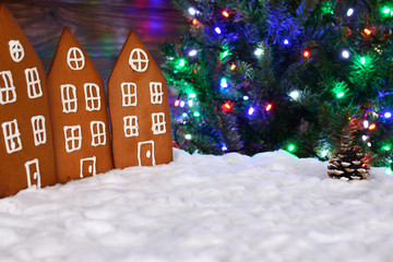 The hand-made eatable gingerbread houses, snow decoration, New Year Tree with garland in background