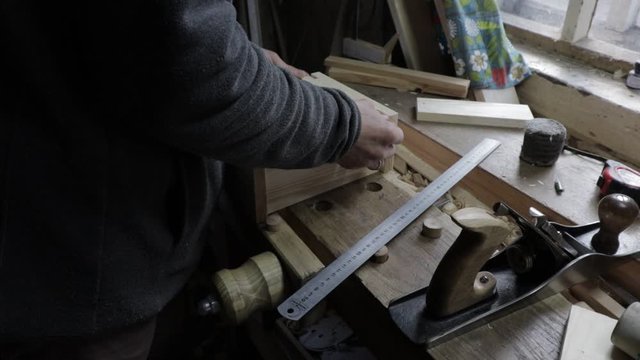 Male carpenter planing of a wooden plank with a jack-plane for pine shelf