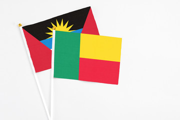 Benin and Antigua and Barbuda stick flags on white background. High quality fabric, miniature national flag. Peaceful global concept.White floor for copy space.