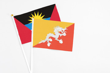 Bhutan and Antigua and Barbuda stick flags on white background. High quality fabric, miniature national flag. Peaceful global concept.White floor for copy space.