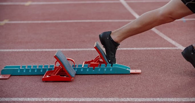 An athlete is getting ready for sprinting, putting feet in starting blocks, then blasting off - professional sports concept 4k footage