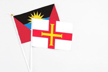 Fototapeta premium Guernsey and Antigua and Barbuda stick flags on white background. High quality fabric, miniature national flag. Peaceful global concept.White floor for copy space.