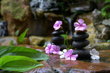 Fototapeta na wymiar Stack of zen stones with flowers next to a garden mini waterfall