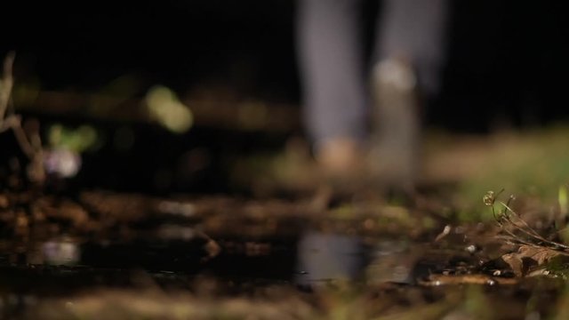 Mysterious man walks into the distance into the dark, stepping into the mud and puddle, close-up of shoes and legs