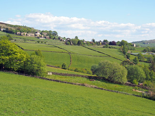 Fototapeta premium sunlit spring countryside with hillside fields and stone walls with the village of old town in calderdale west yorkshire