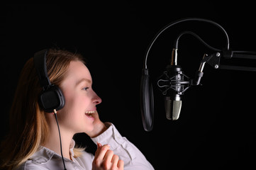 Female vocal recording. Young girl with microphone and headphones in recording studio. Recording of...