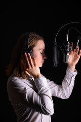 Recording female vocals. Young girl with a microphone and headphones in a recording studio....