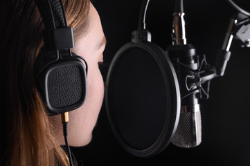 Female vocal recording. Young girl with microphone and headphones in recording studio. Recording of...