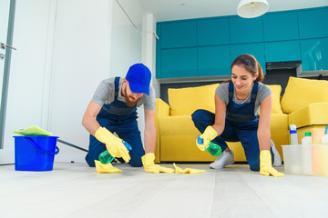 Smiling girl and handsome bearded man in workwears washing the parquet with the cleaning items and wipping with rags