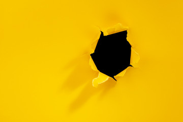 Torn hole in yellow paper background.