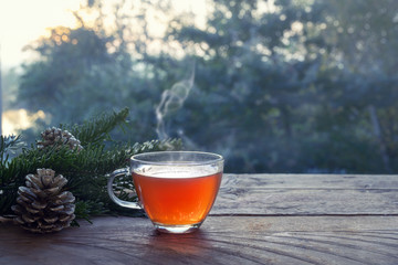 Cup with hot steaming tea on a rustic wooden garden table with Christmas decoration on a winter...