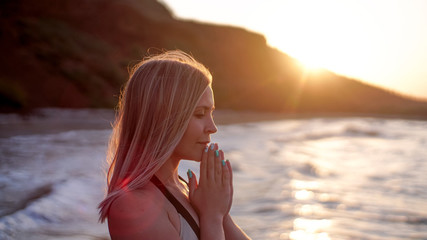 Beautiful woman prays on the sea shore on the sunset