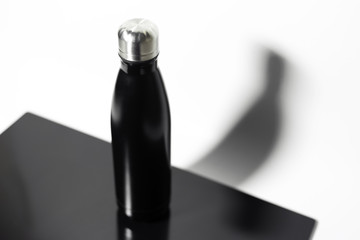 Top view of black steel thermo eco bottle for water, on black glass table, background of white.