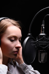 Recording female vocals. Young girl with a microphone and headphones in a recording studio....