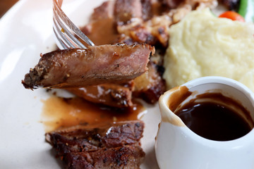 Close-up piece sliced of premium quality Australia Beef Steak in the fork with black pepper sauce in white plate background. Foods concept.