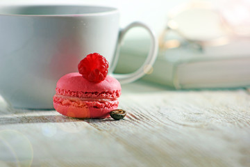 Multicolored macaroons on a wooden table, cookies with raspberries, on the background of mugs and books,  confectionery, toned
