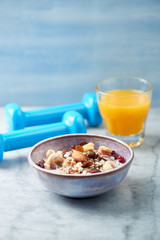 Bowl of granola with yogurt, nuts, raisins, cranberries and chia seeds. Blue dumbbells in background. Concept for a tasty and healthy meal. Stone - wooden background. Close up.