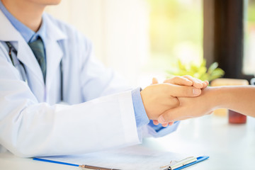 Friendly man doctor's hands holding male patient's hand for encouragement and empathy. Partnership, trust and medical ethics concept. Bad news lessening and support. Patient cheering and support
