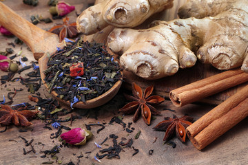 black blended tea, ginger, anise and cinnamon on a wooden table. tea in a wooden spoon and...