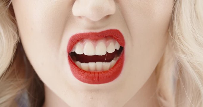 Close up shot of girl wearing makeup with red lipstick and perfect teeth doing a seductive growl - emotions concept 4k footage