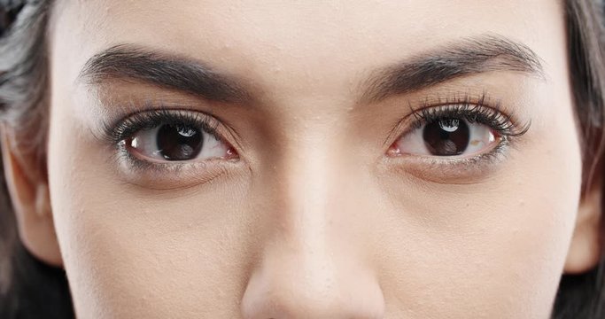 Close up shot of female eyes with makeup on eyelashes and dark brown irises looking around, isolated on black background 4k footage