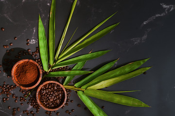 coffee background of roasted coffee beans and grounded coffee powder in wooden cups with green leaves on black marble background
