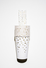 Row of paper  disposable cups with straws   with golden dots with a bottle of champagne , top view over a white bacjkgrpund, hard light with rounded shadow
