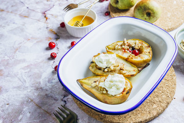 Sweet baked pears with honey, nuts, cranberries and cinnamon in enameled baking bowl on stone background. Top view. Flat lay