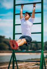 Obraz premium Fit man working out at the beach on chin up bar