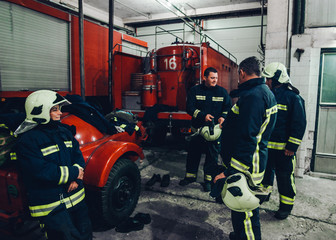 Fototapeta na wymiar Team of smiling firefighters conversing by firetruck at station