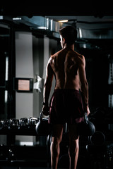 Fototapeta na wymiar Slim muscular man lifting weights in the gym