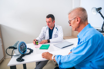 Serious middle aged doctor prescribes his senior patient the medication he is supposed to buy and use for his health, while sitting in his office.
