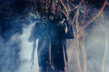 Portrait of the angel of death, grim reaper while standing in a mystical wood at night.