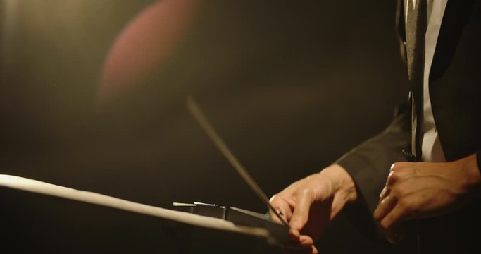 Close up shot of hands of symphony orchesra conductor directing music by waving his baton. Studio shot on black background 4k footage