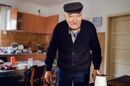 Senior Man Grandfather Old Pensioner Farmer Wearing Black Sweater And Hat Having A Cup Of Coffee Or Tea Cooking In The Pot At Home Waiting To Boil