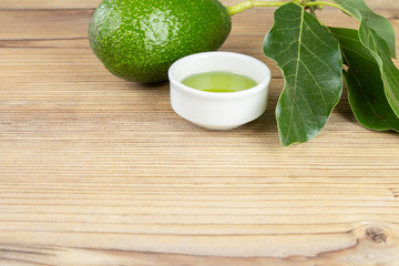Fresh organic avocado oil. Avocado with leafs on wooden table and cup of oil. Copy space for text. Natural ingredients.