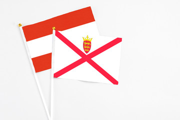 Fototapeta premium Jersey and Austria stick flags on white background. High quality fabric, miniature national flag. Peaceful global concept.White floor for copy space.