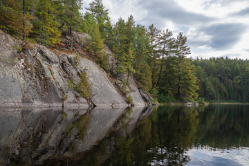 Fototapeta na wymiar Smooth rock slope with trees reflected in still water