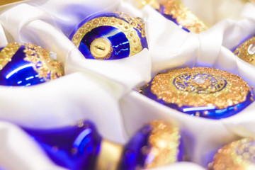 Fototapeta premium Christmas tree blue balls and with golden ornament and rhinestones on a white silk cloth - closeup soft focus background