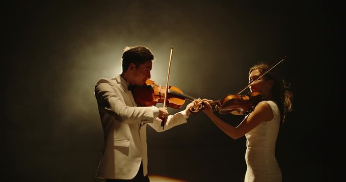 Duet of two professional violin players having a solo together, performing on stage during concert, spotted by light on black background 4k footage