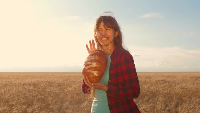 loaf of wheat bread in the hands of a happy woman, over field of wheat. Fresh rye, crisp bread is held in the hands of a farmer. tasty piece of bread on the palms of the baker.