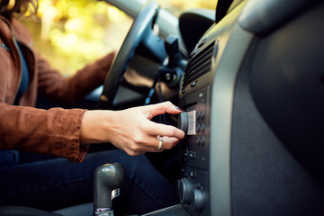 Unrecognizable woman turning button on car radio for listening to music