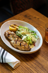 Grilled white fish with lemon and greens on a side inside restaurant 