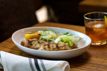 Grilled white fish with lemon and greens on a side inside restaurant 