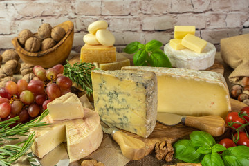 Assortment of cheeses with  herbs, vegetables, nuts and grapes. Food for wine, cheese delicatessen on a wooden board.