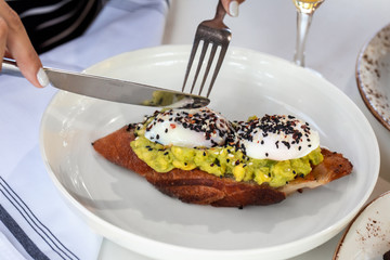 Haute cuisine - grilled sandwich with avocado guacamole sauce and two sunny side up eggs with woman...